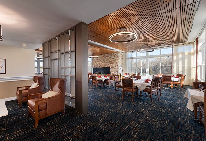 A modern dining area with wooden ceilings and large windows, featuring neatly arranged tables and comfortable seating.