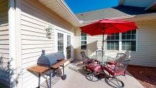 A sunny patio with outdoor furniture, a grill, and a red umbrella.