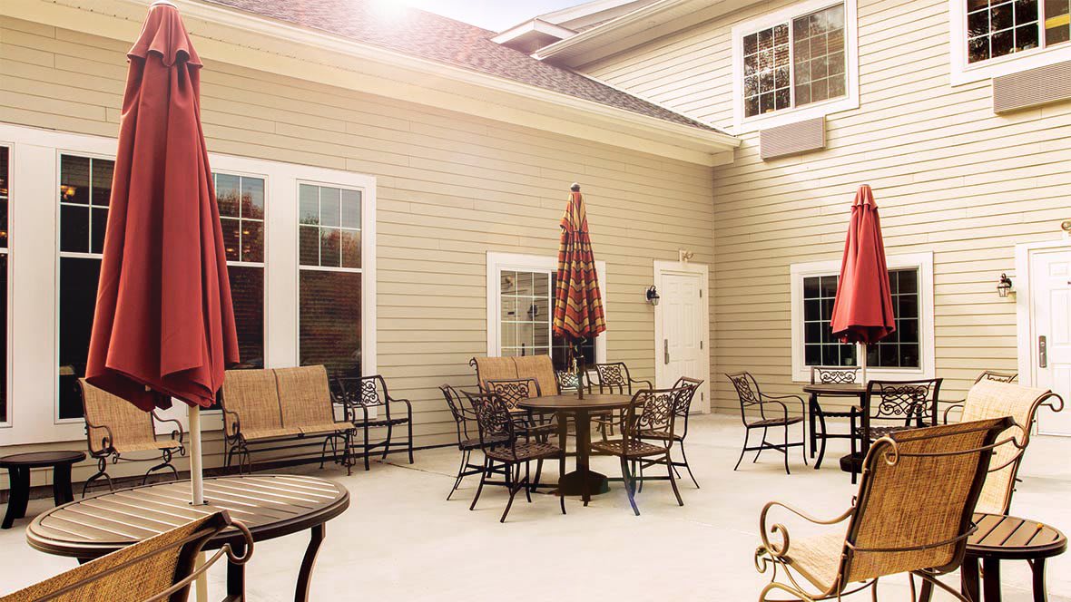 A cozy patio with tables, chairs, and an umbrella under sunlight.