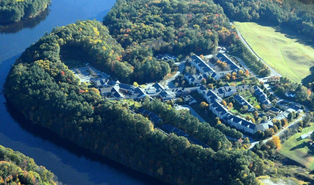 Aerial view of a residential area surrounded by dense forest and a nearby water body.