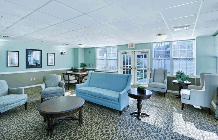 A cozy living room with pastel blue and gray furniture, featuring a sofa, chairs, tables, and large windows.