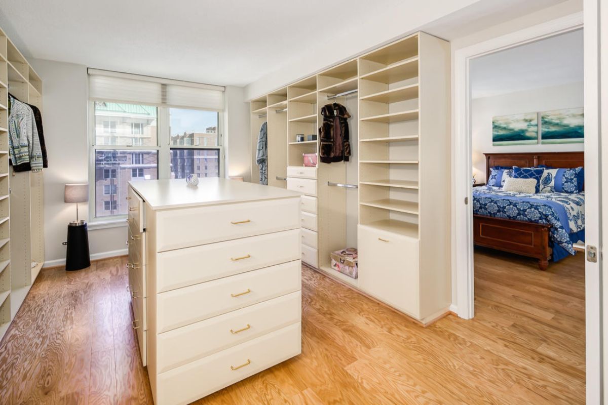 A spacious walk-in closet with built-in shelves and a central dresser, featuring modern design and wood flooring.