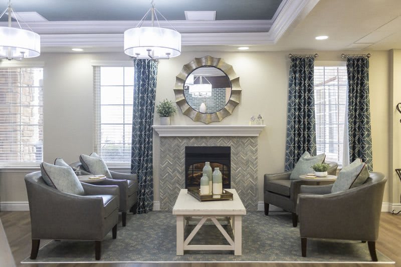 A modern living room with a stylish fireplace, elegant armchairs, and a decorative mirror.