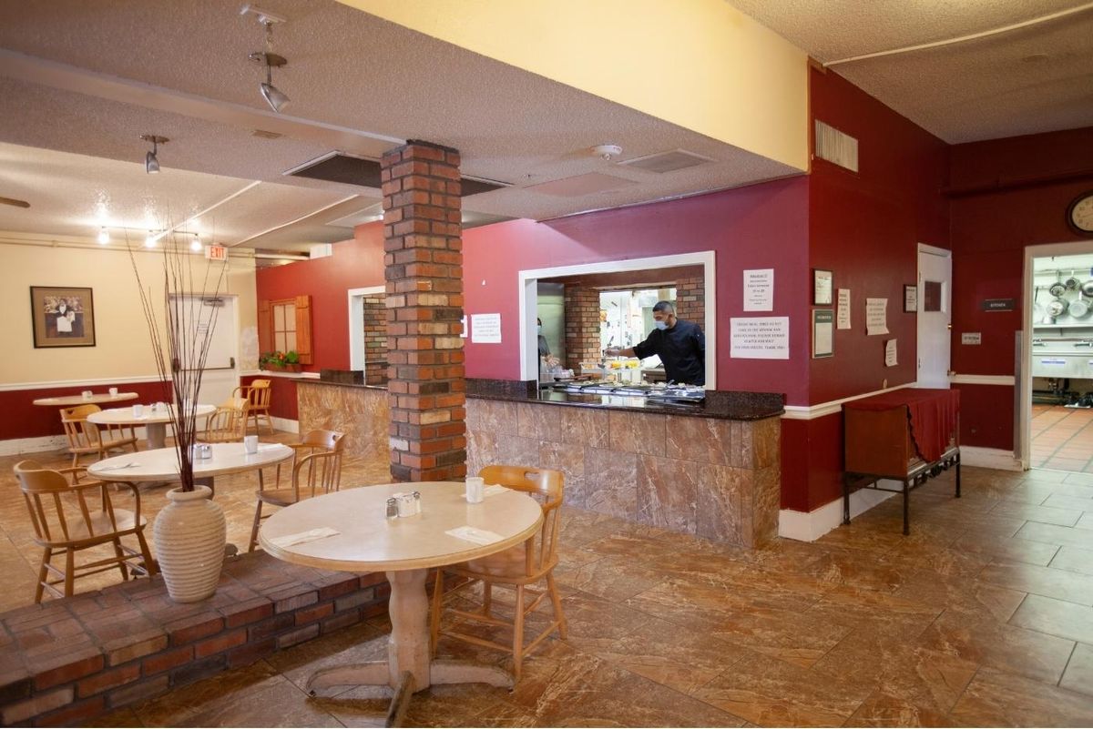 A cozy restaurant interior with tables, chairs, a brick column, and a serving counter against red walls.