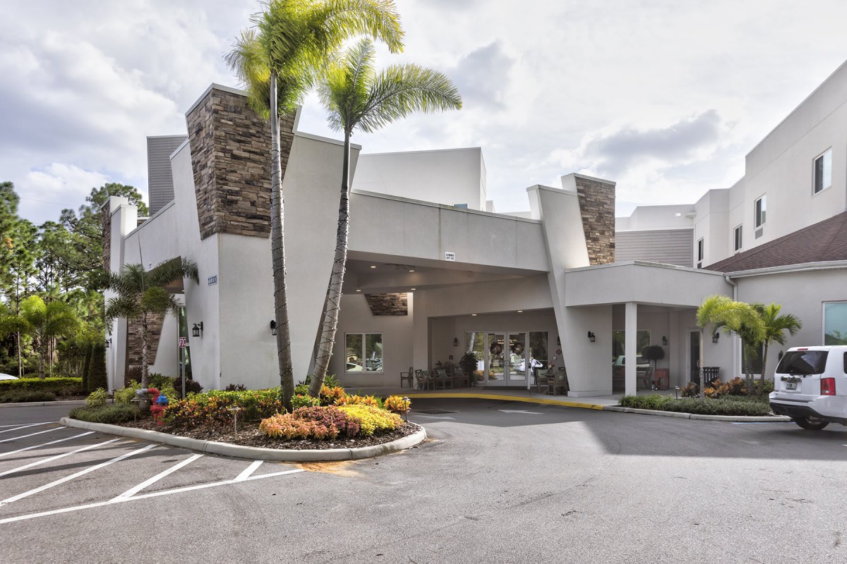 Modern hotel entrance with landscaped surroundings and palm trees.