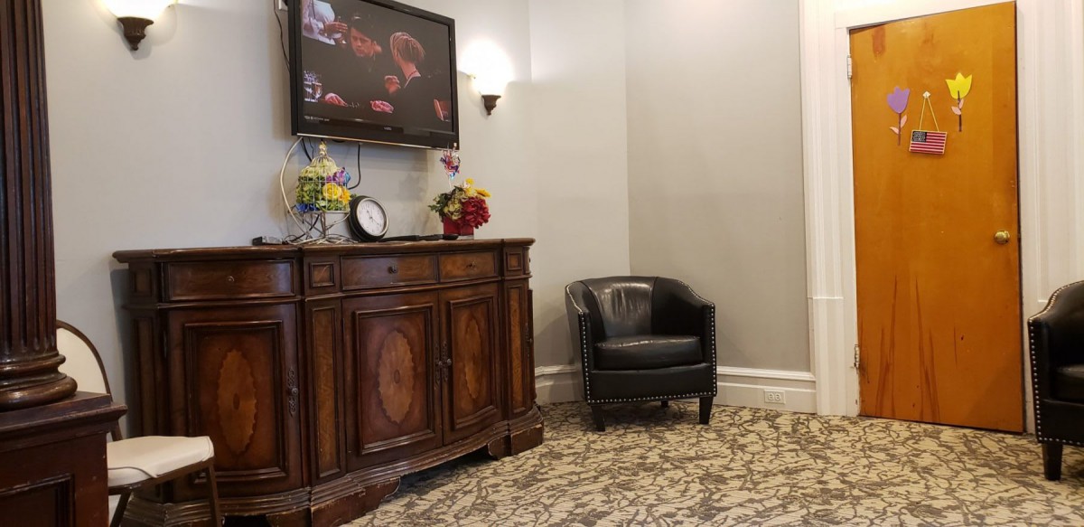 A waiting room with a leather armchair, a decorative cabinet, and a wall-mounted television.