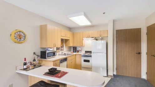 A modern kitchen interior with light wood cabinets and various appliances, including a refrigerator and microwave.