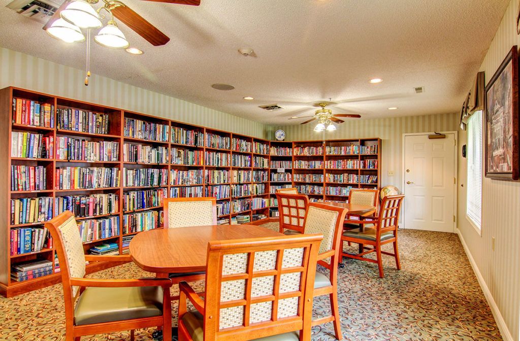 A cozy library with wooden tables and chairs surrounded by bookshelves filled with books.