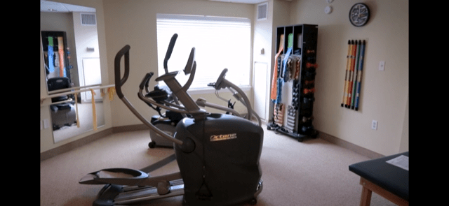 A compact fitness room featuring two elliptical machines and a rack of exercise mats.