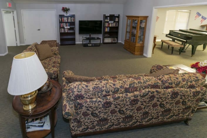A cozy living room with patterned sofas, a television, bookshelves, and carpeted flooring.