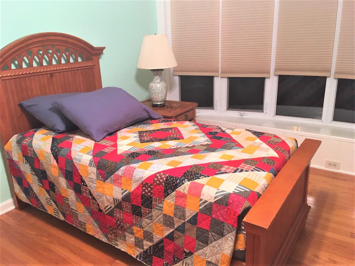 A cozy bedroom with a colorful quilt on the bed, next to a nightstand with a lamp.