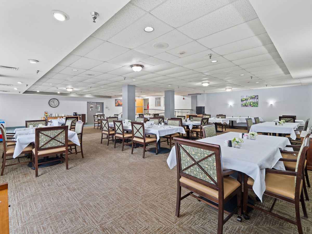 A spacious dining room with multiple tables set for service, featuring white tablecloths and comfortable seating.