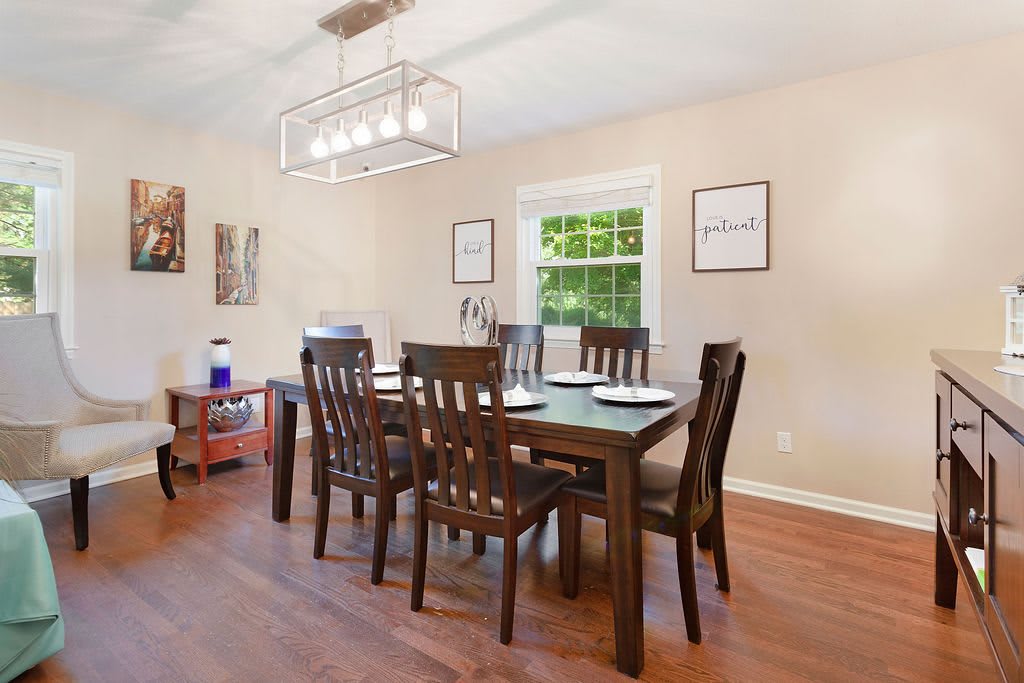 A modern dining room with a wooden table and chairs, featuring a large window and decorative artwork on the walls.