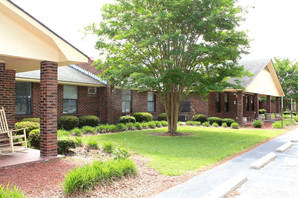 A brick house with a well-maintained front yard featuring a tree and landscaped greenery.