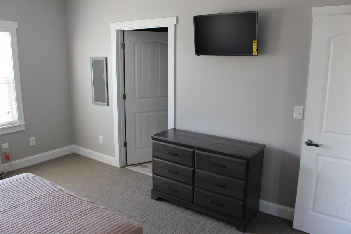 A minimalist bedroom featuring a wall-mounted television and a gray dresser.