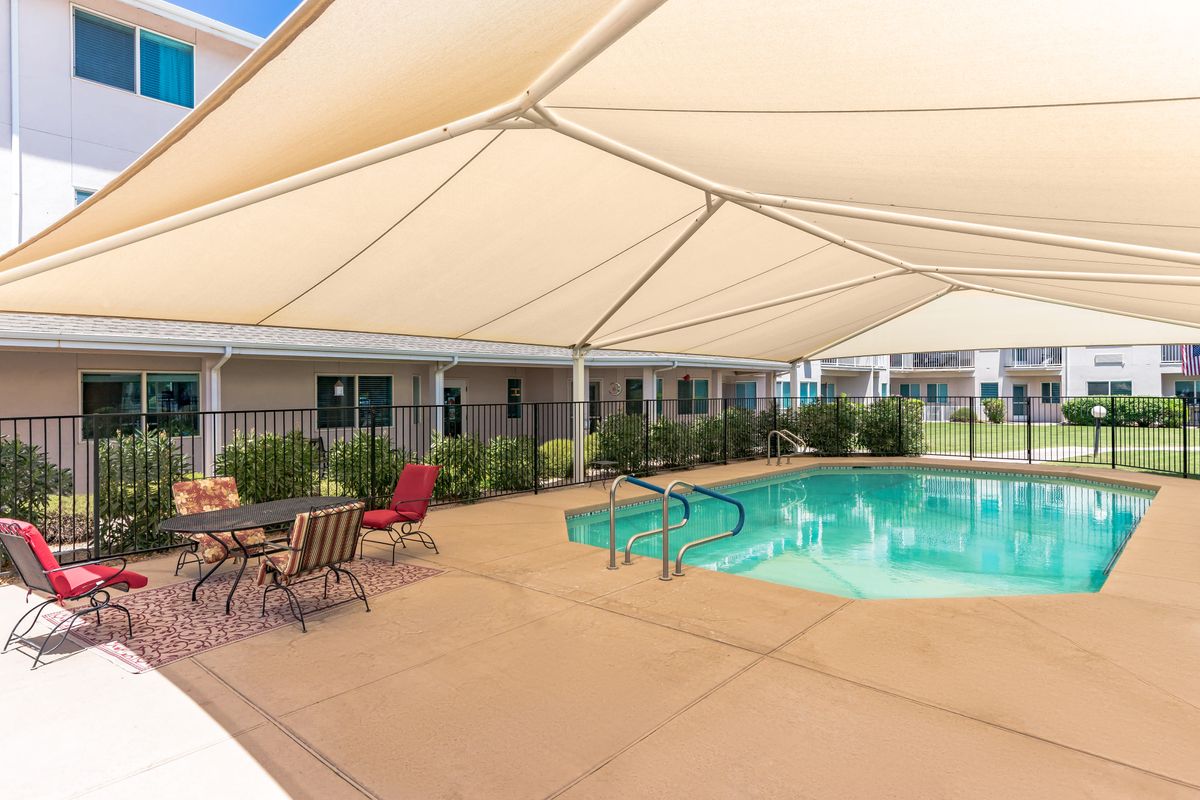 An outdoor swimming pool with a shaded seating area and a protective fence.