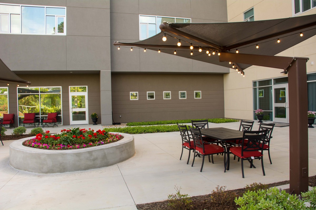 A cozy outdoor patio area with tables, chairs, and string lights next to a building.