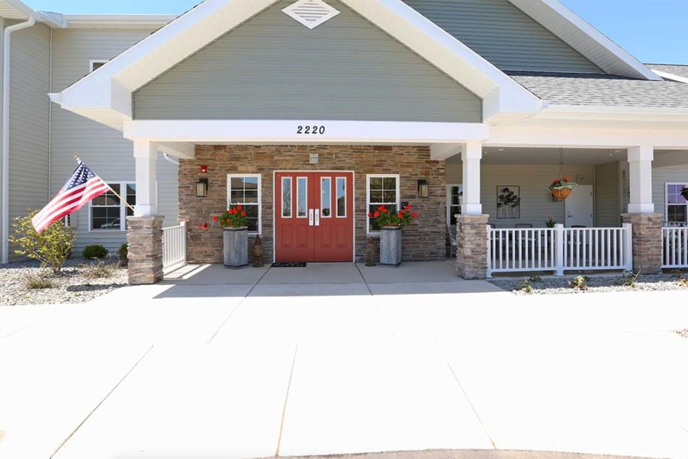 A welcoming building entrance with red double doors, adorned by flowers and supported by stone pillars.