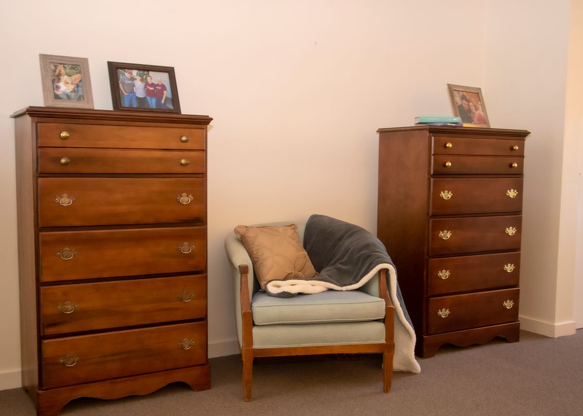 A cozy room with two wooden dressers and an upholstered chair adorned with cushions.