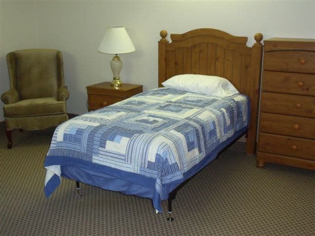 A neatly made single bed with a patterned quilt, alongside a nightstand and lamp.
