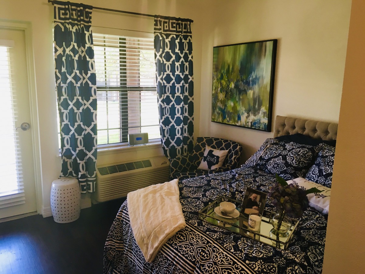 A cozy bedroom interior featuring patterned curtains, a decorated bed, and a large painting on the wall.