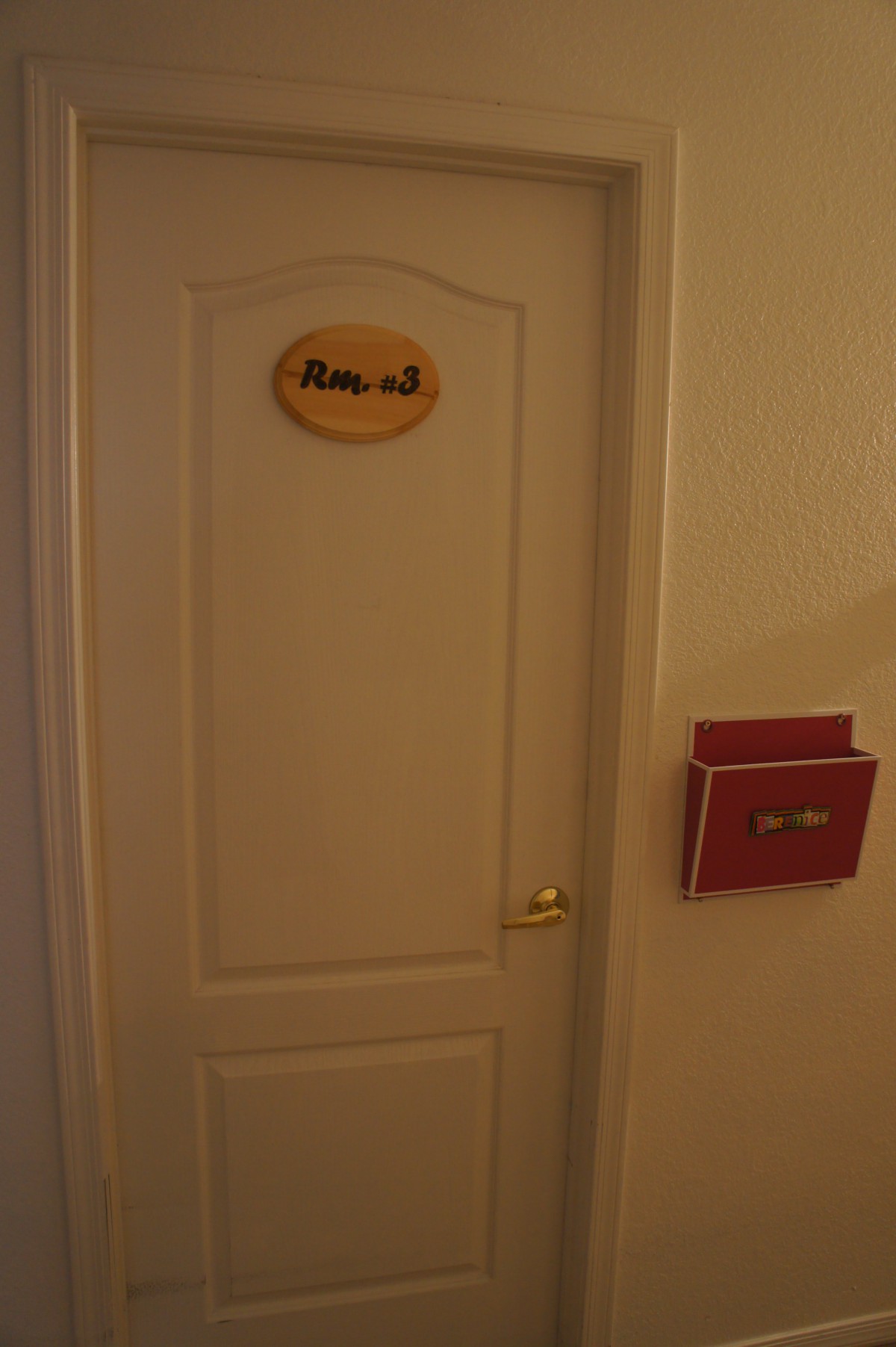 A hotel room door with a room number sign and a folder on the wall.