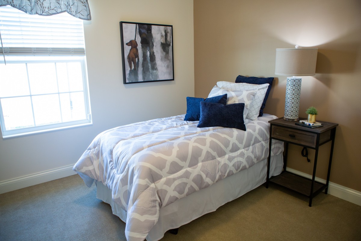 A neatly arranged bedroom with a single bed, decorative pillows, and artwork on the wall.