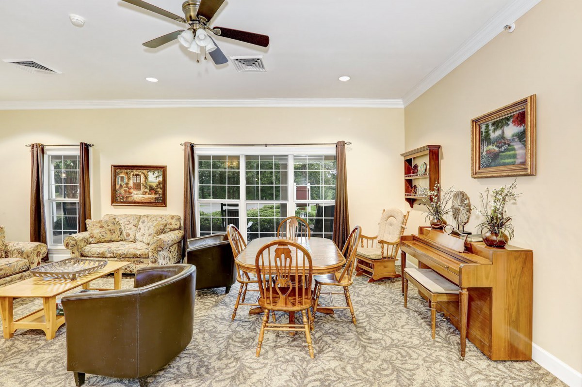 A cozy living room featuring comfortable seating, a wooden dining table, decorative elements, and a large window allowing natural light.