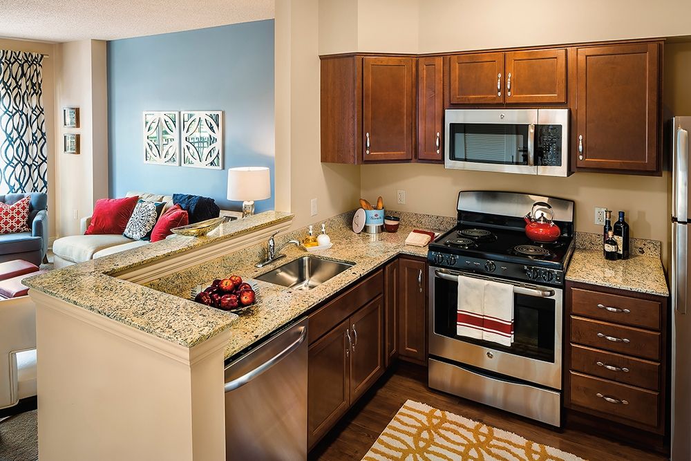 A modern kitchen with stainless steel appliances, wood cabinets, and a granite countertop.