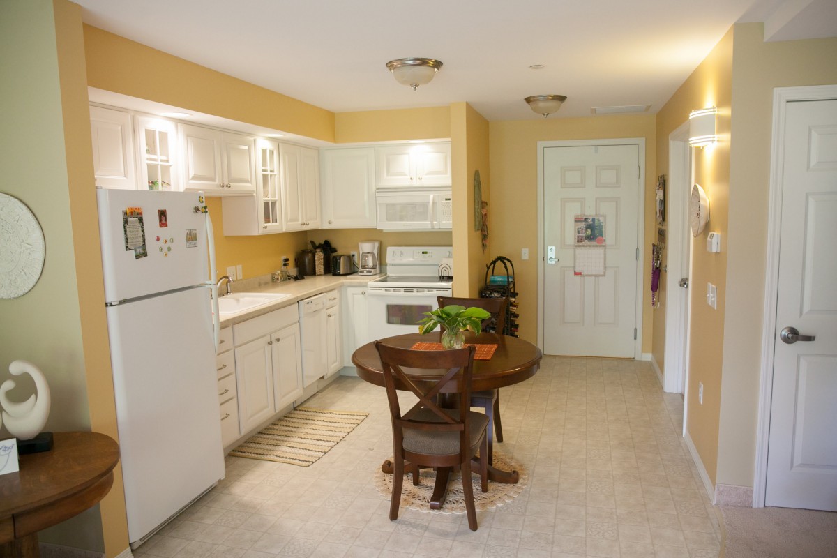 A cozy kitchen with white cabinets, yellow walls, and a round dining table.