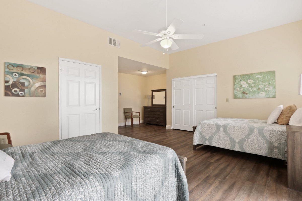 A spacious modern bedroom with two beds, a ceiling fan, and wooden flooring.