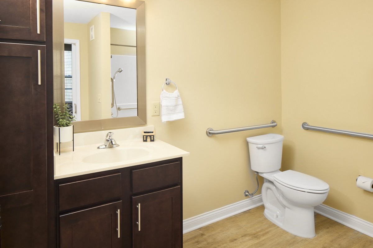 A modern bathroom featuring a sink, toilet, and mirror with light yellow walls.