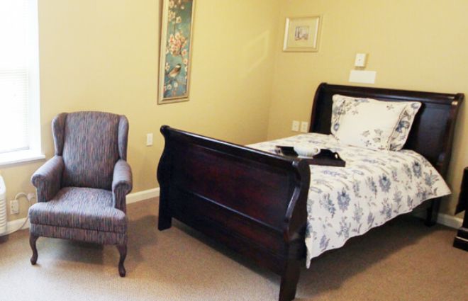 A traditional bedroom with a dark wood bed and an upholstered chair.
