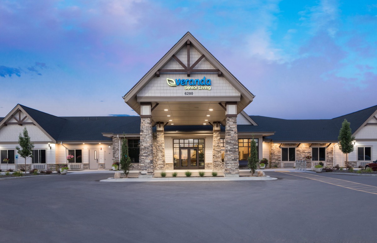 The exterior entrance of a commercial building with a peaked roof and stone columns against a clear sky.