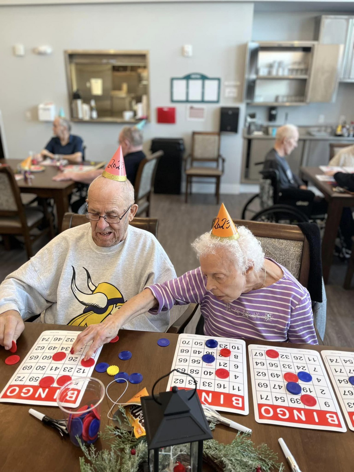 Elderly individuals enjoying a game of bingo while wearing party hats at a community center.