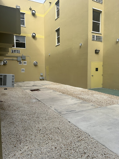 A view of a courtyard featuring yellow walls, paved surfaces, and air conditioning units in an urban setting.
