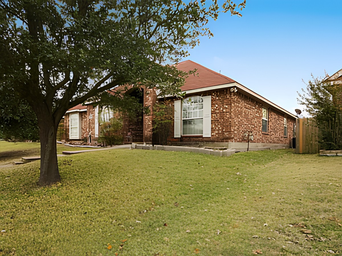 A suburban brick house with a spacious front yard and a tree.