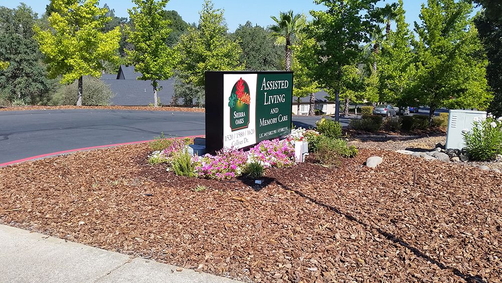 A well-maintained landscape featuring a business sign surrounded by greenery and flowers near a parking area.