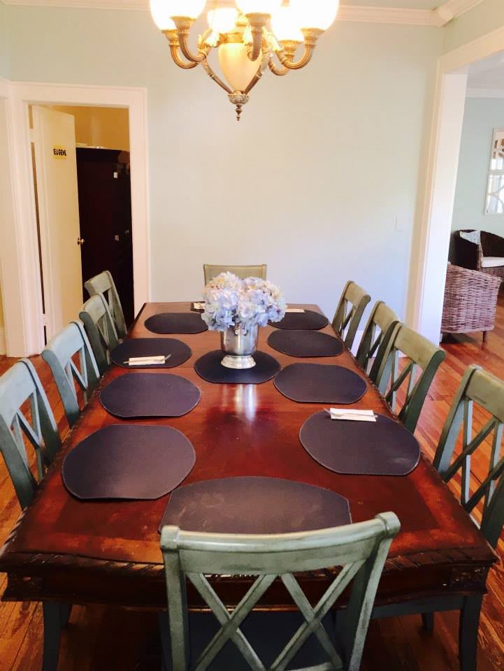 A spacious dining room with a large wooden table set with placemats and surrounded by chairs.