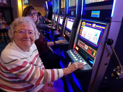 An older woman enjoys her time playing slot machines at a casino.