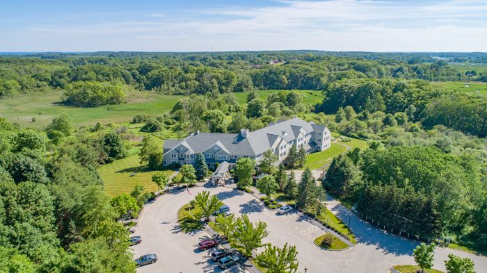 Aerial view of a building surrounded by lush greenery and a parking lot on a sunny day.
