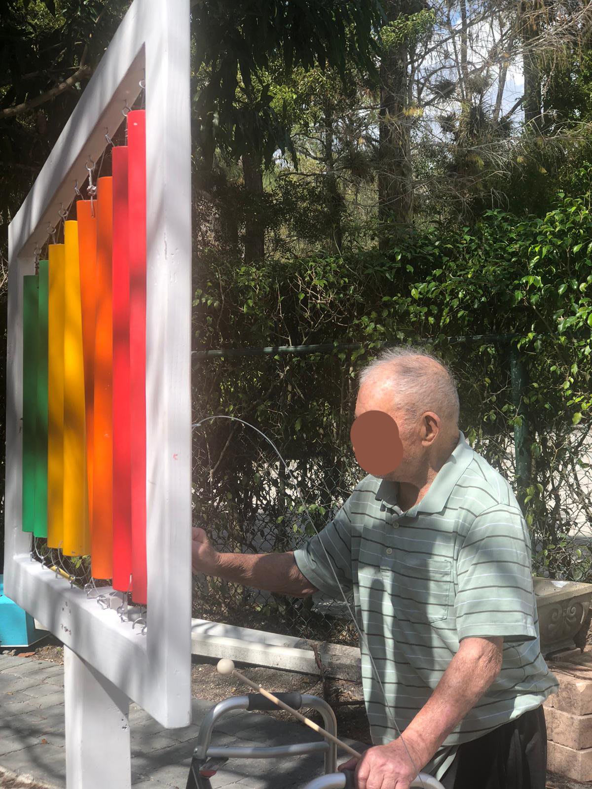 An elderly person playing a colorful outdoor xylophone in a park.