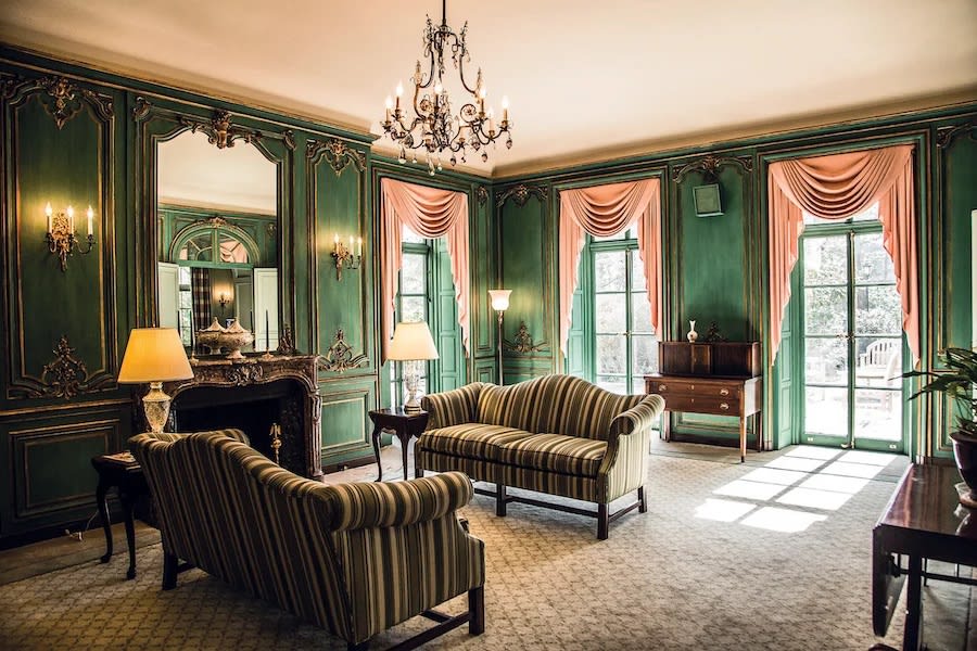 A vintage-style living room with green wall panels, elegant furniture, and a chandelier.