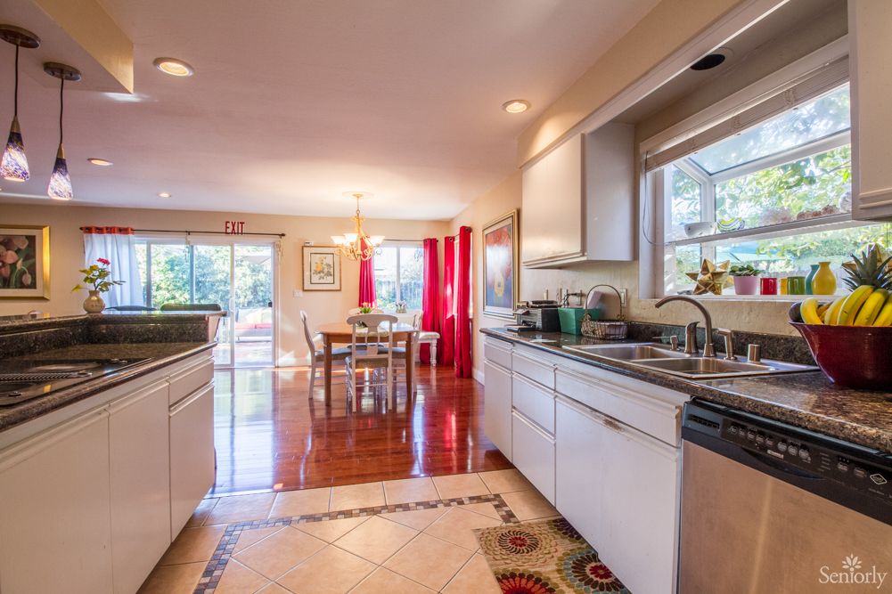 A modern kitchen and dining area with white cabinets and wooden flooring, illuminated by natural light.