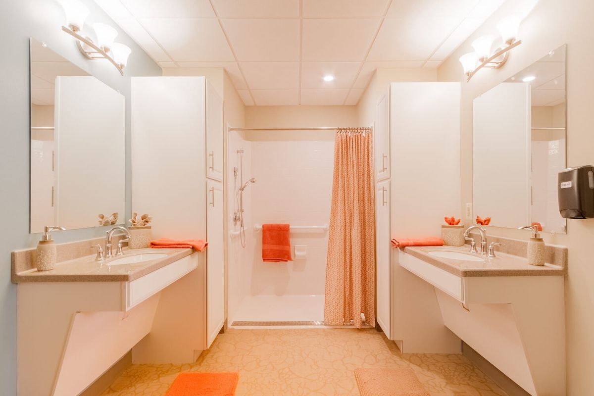 A modern bathroom with double sinks and orange accents, featuring clean and minimalistic design.