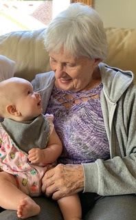 A grandmother lovingly holds her smiling grandchild on a couch.