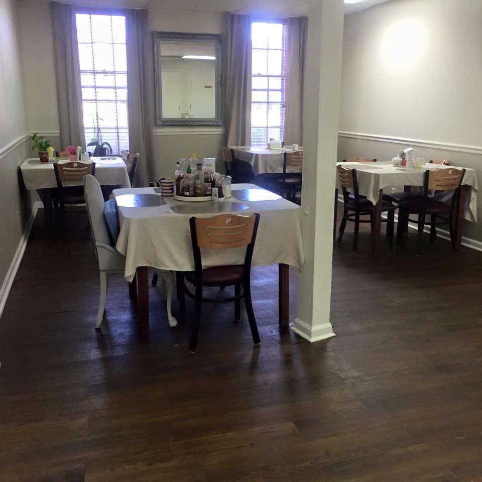 A dining area with several tables covered in white tablecloths, surrounded by chairs.