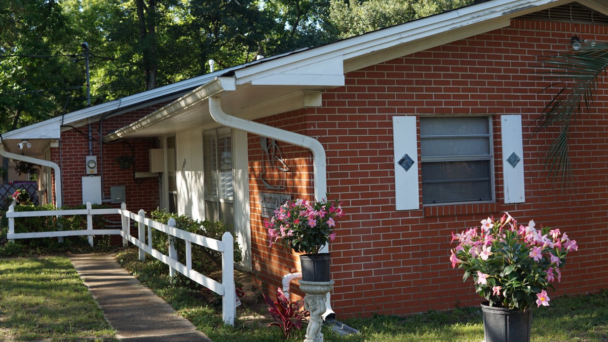 A brick house with a white fence and colorful flowers in the yard.