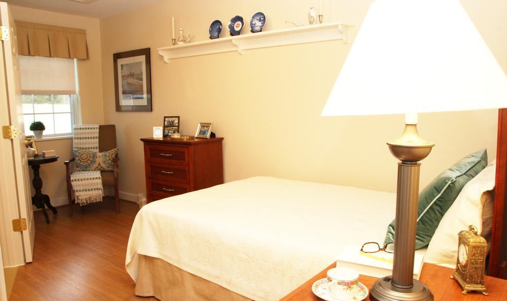 A cozy bedroom with a neatly made bed, a lamp on the bedside table, and various decorative items.