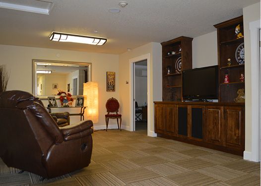 A cozy living room featuring a leather recliner, built-in wooden shelves with a television, and a warm lighting setup.